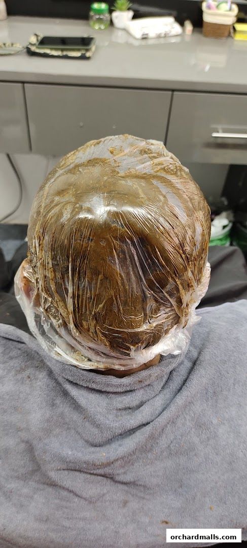 A person's head covered in hair dye and plastic wrap, ready for treatment.