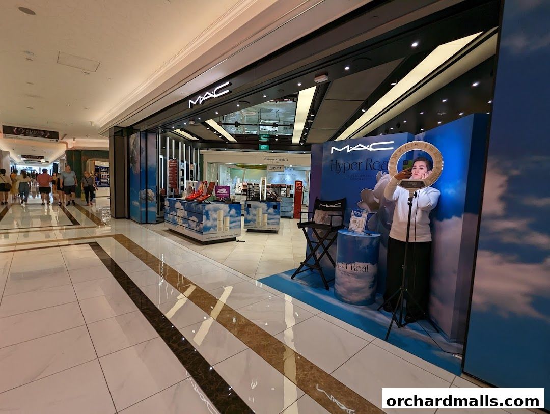 MAC Cosmetics store entrance with a promotional display and a person using a ring light.