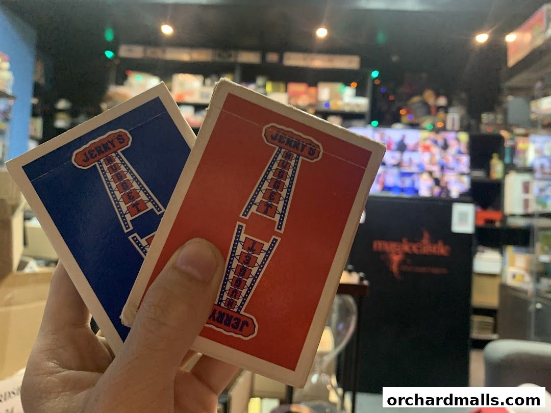 A hand holds two decks of Jerry's Nugget playing cards in front of a magic shop.