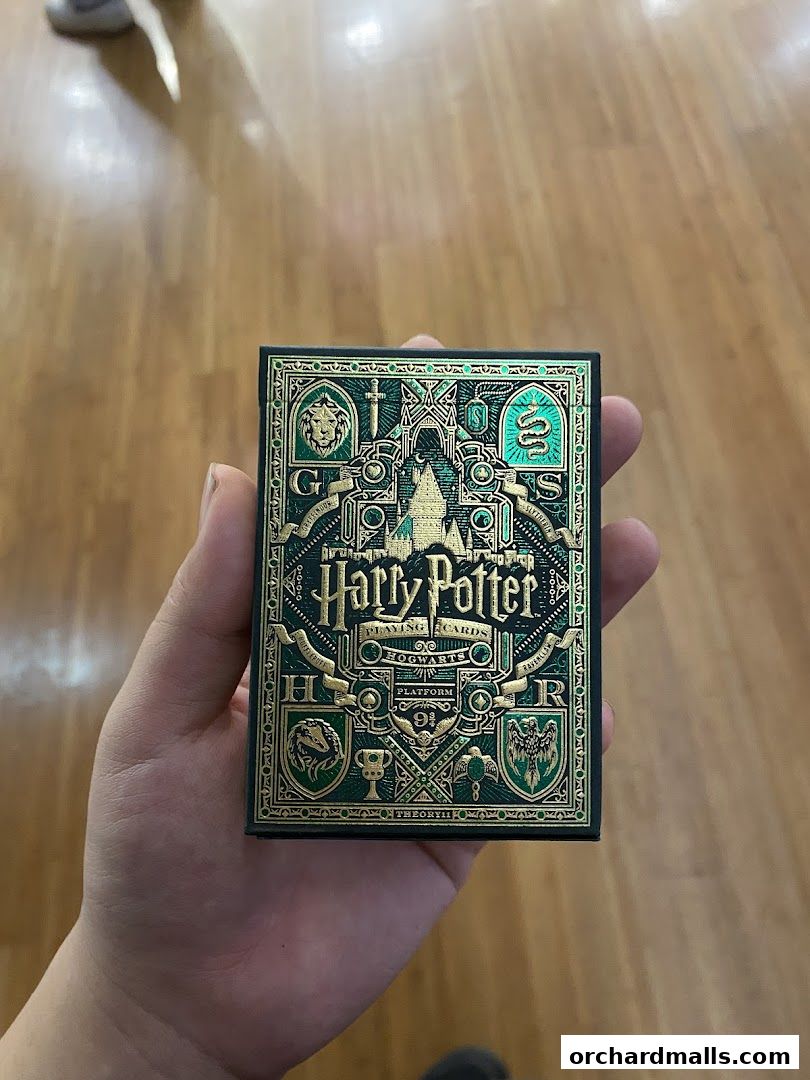 A hand holds a deck of Harry Potter themed playing cards with intricate gold and green designs.