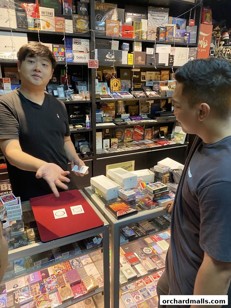 A man demonstrates a magic trick with cards in a shop filled with magic supplies.