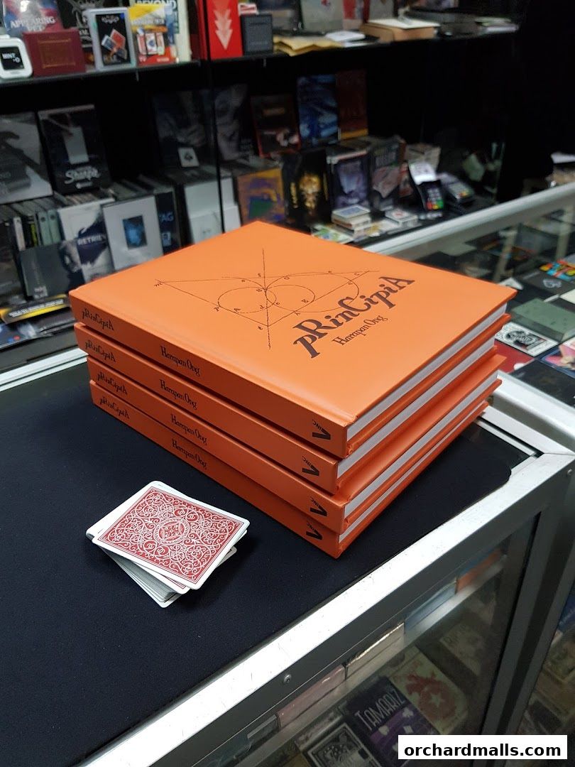 Stack of orange books titled 'Principia' and a deck of cards on a display counter.