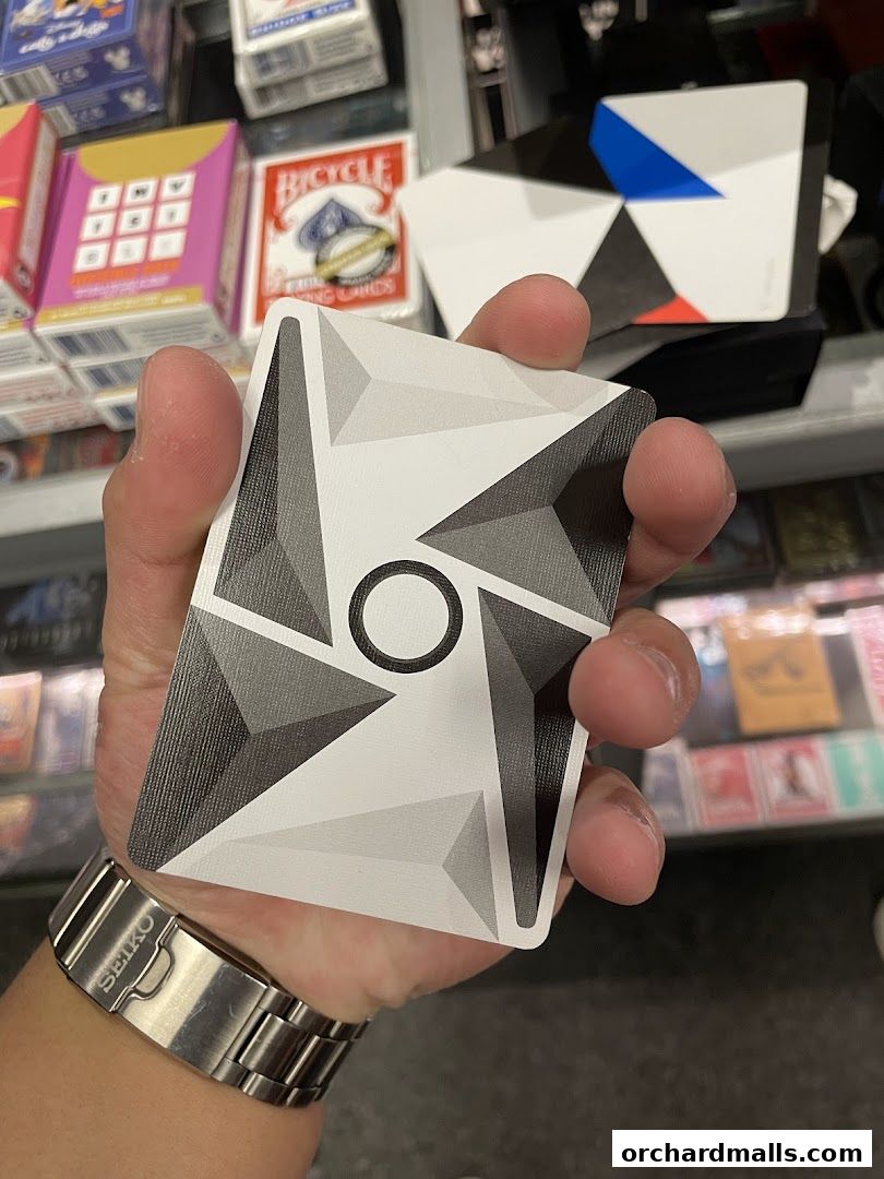 A hand holds a deck of cards with a geometric design, surrounded by other card decks.