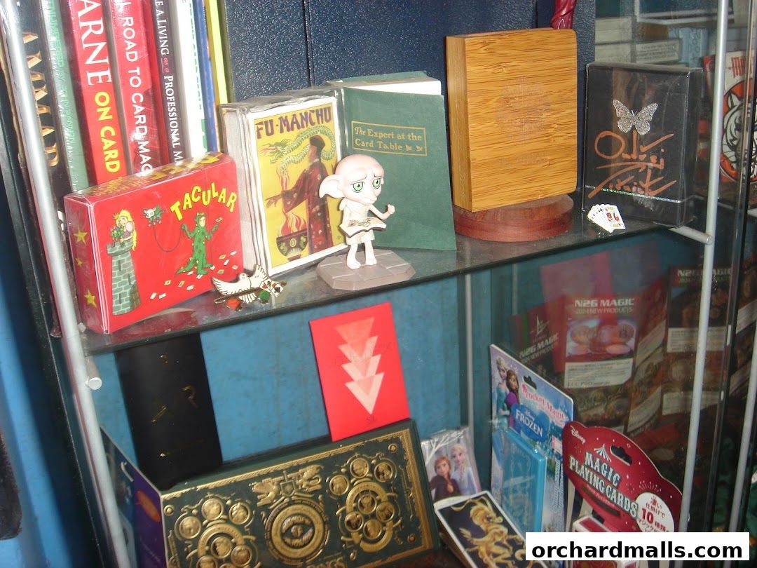 A display shelf filled with magic trick boxes, playing cards, and books.