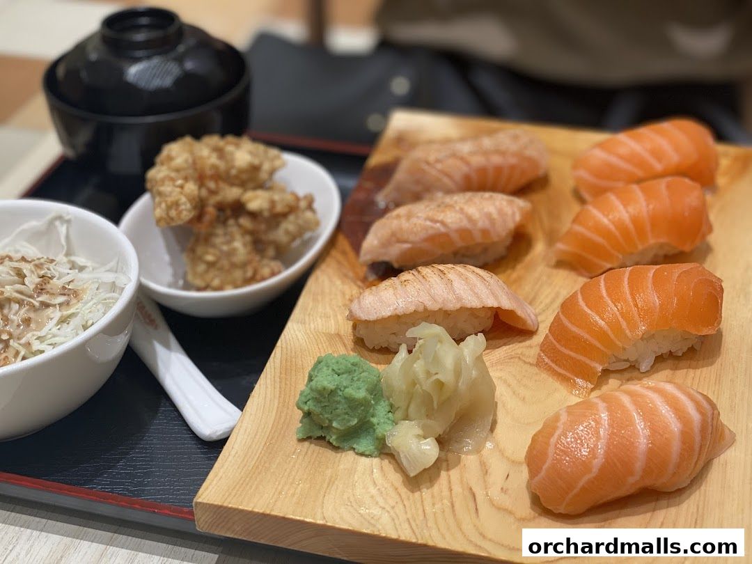 A wooden platter of salmon sushi, fried chicken, and a side salad with soup.