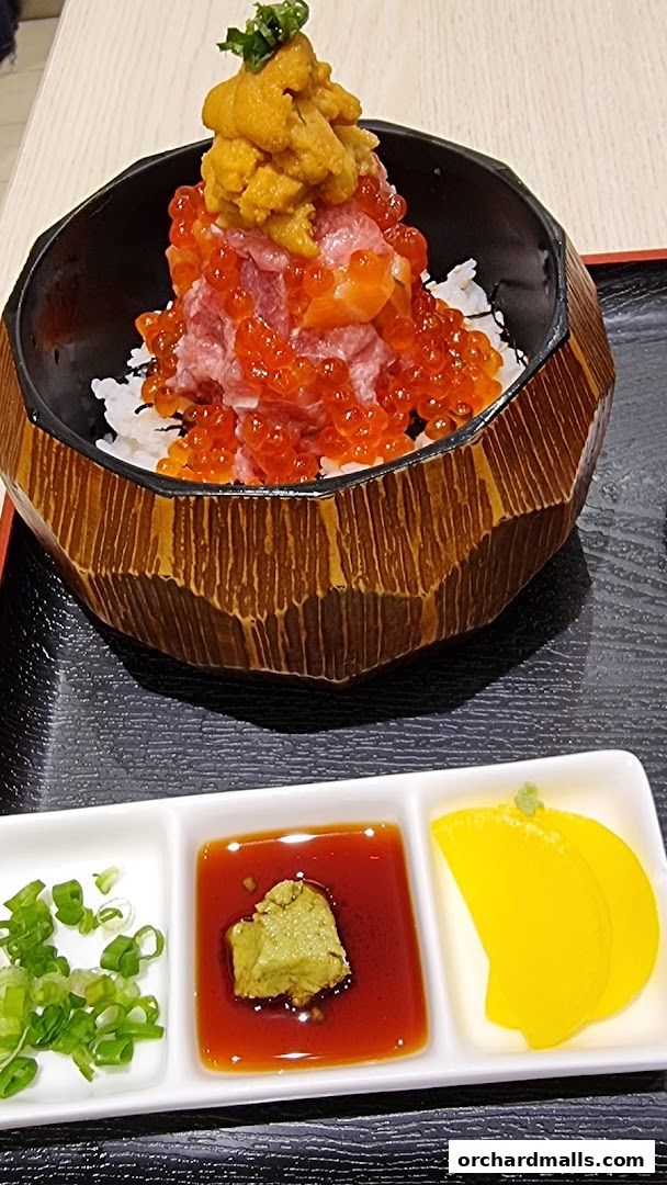 A bowl of rice topped with tuna, salmon, ikura, and uni, served with condiments.