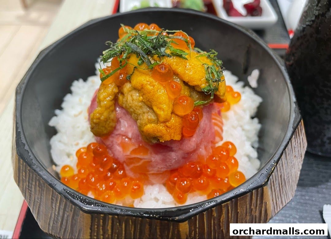 A close-up of a delicious seafood rice bowl topped with uni, ikura, and tuna.