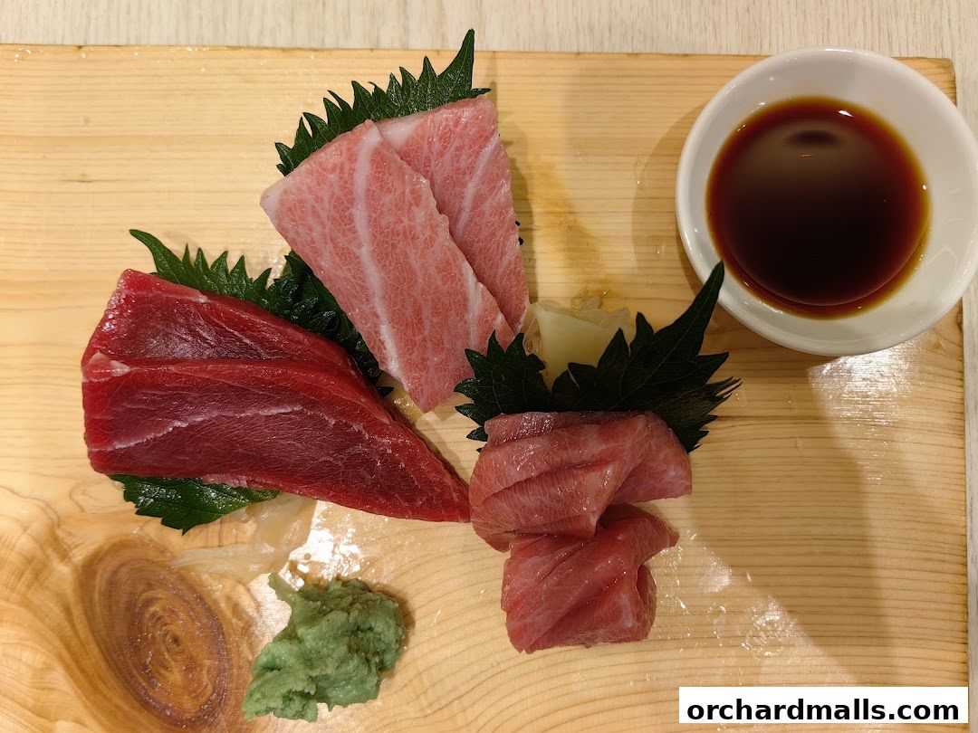 Fresh tuna sashimi served with soy sauce, wasabi, and ginger on a wooden board.