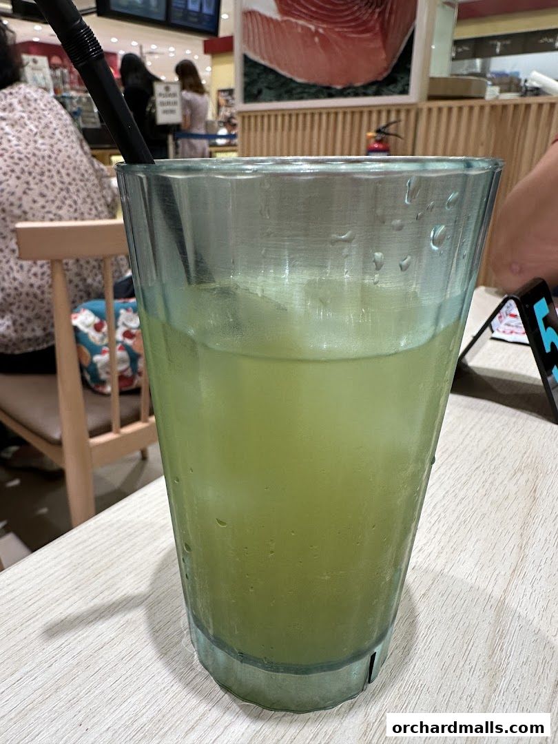 A refreshing green beverage with ice and a straw in a glass on a wooden table.