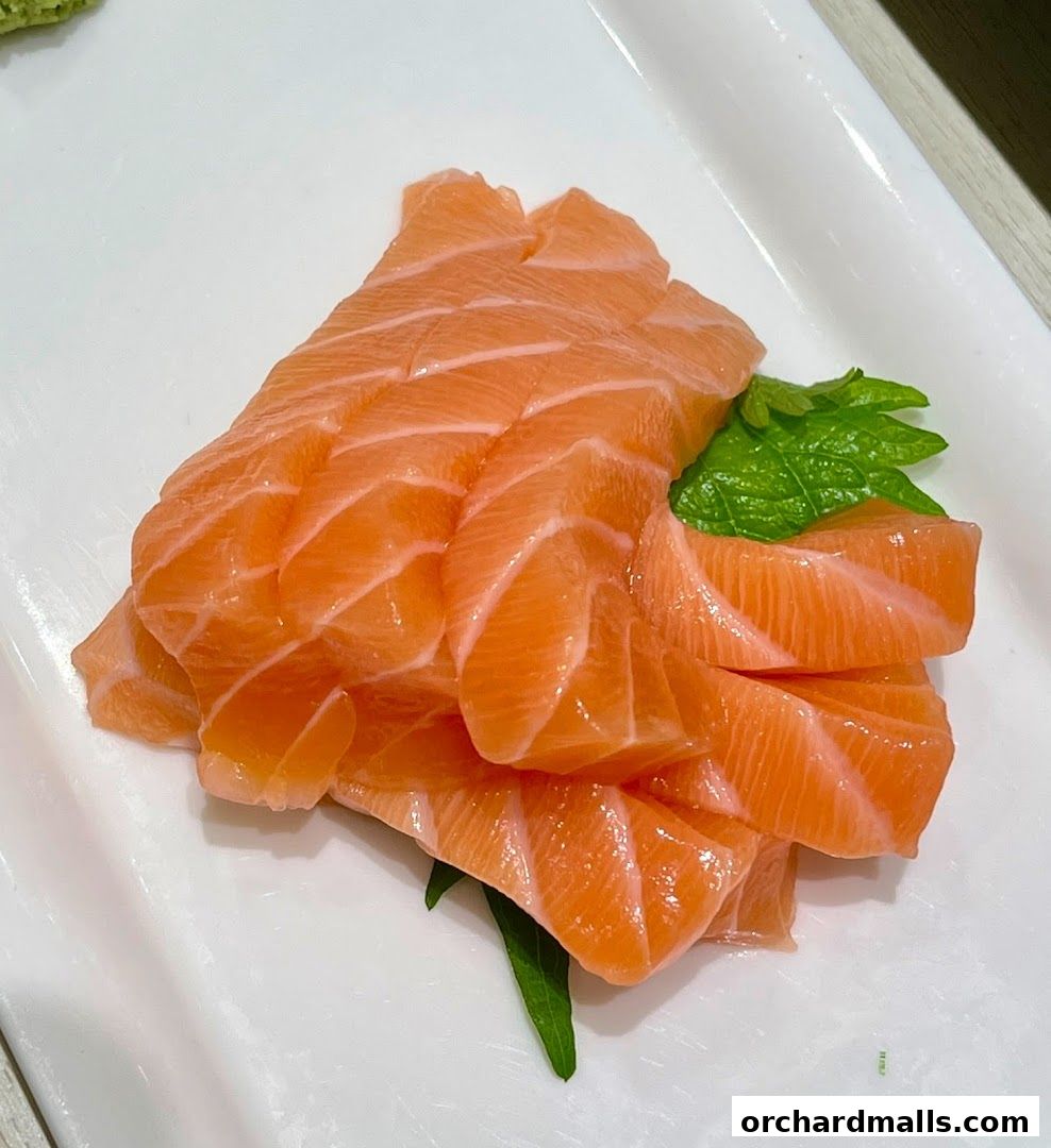 Freshly sliced salmon sashimi served on a white plate with a garnish.