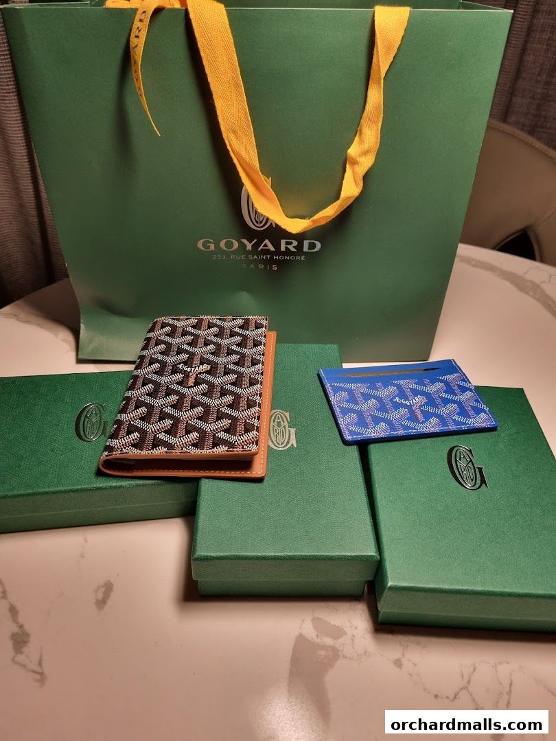 Goyard shopping bag with luxury accessories and gift boxes on a marble table.