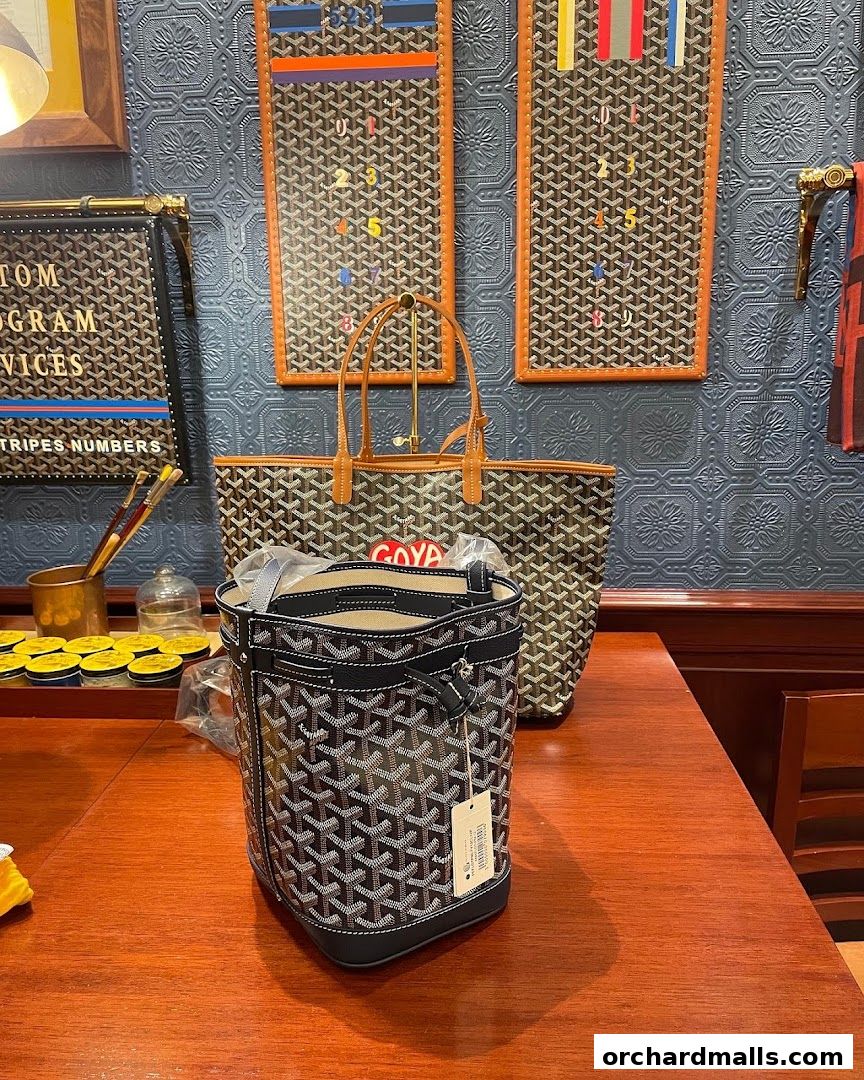 Goyard handbags displayed on a wooden table with patterned wallpaper.