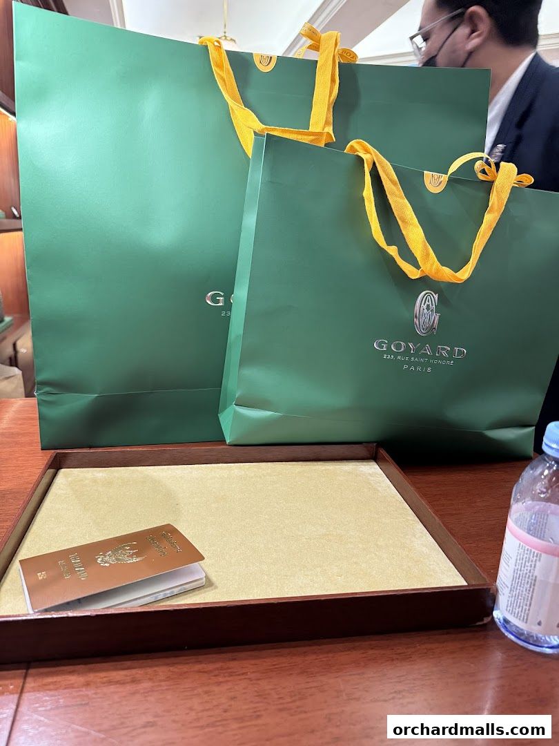 Goyard shopping bags and a passport on a wooden counter.