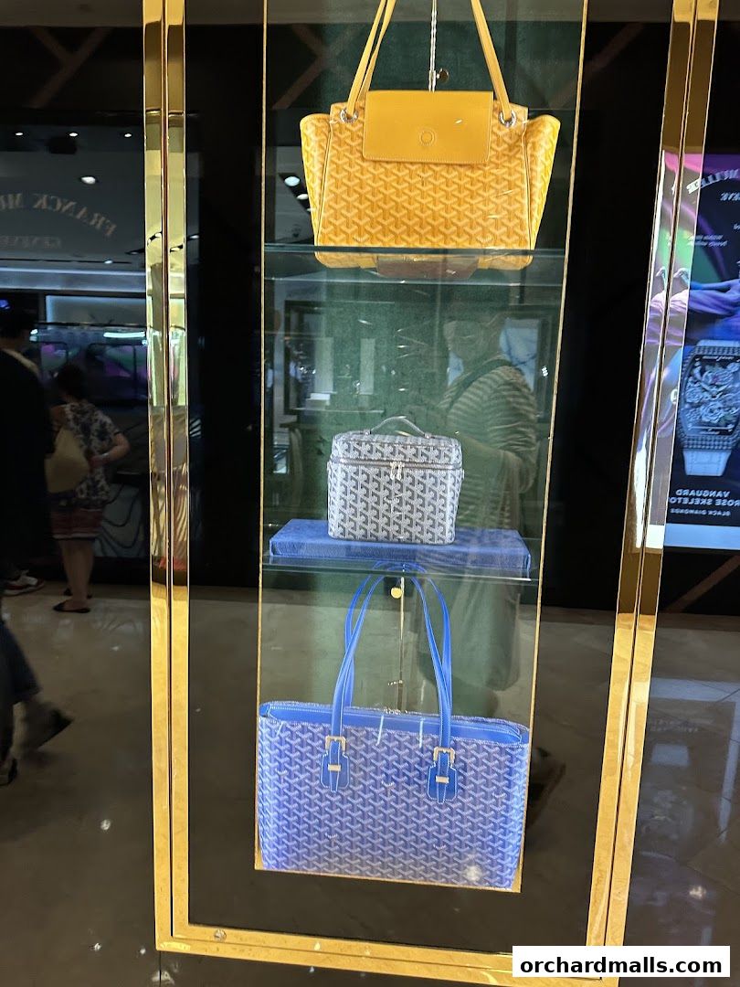 Goyard handbags displayed in a luxury store window with gold trim.
