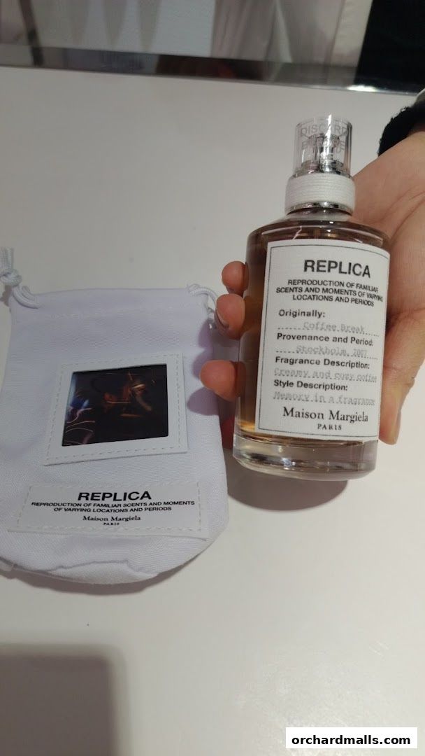 A hand holds a Maison Margiela 'REPLICA' perfume bottle and its pouch.