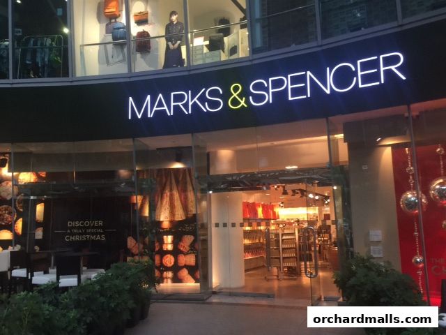 The exterior of a Marks & Spencer store with a prominent illuminated sign and festive window displays.