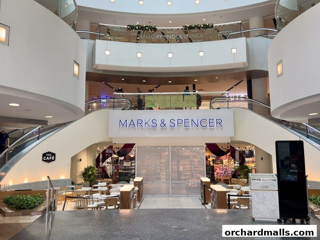 Marks & Spencer store entrance with a cafe area and escalators in a shopping mall.