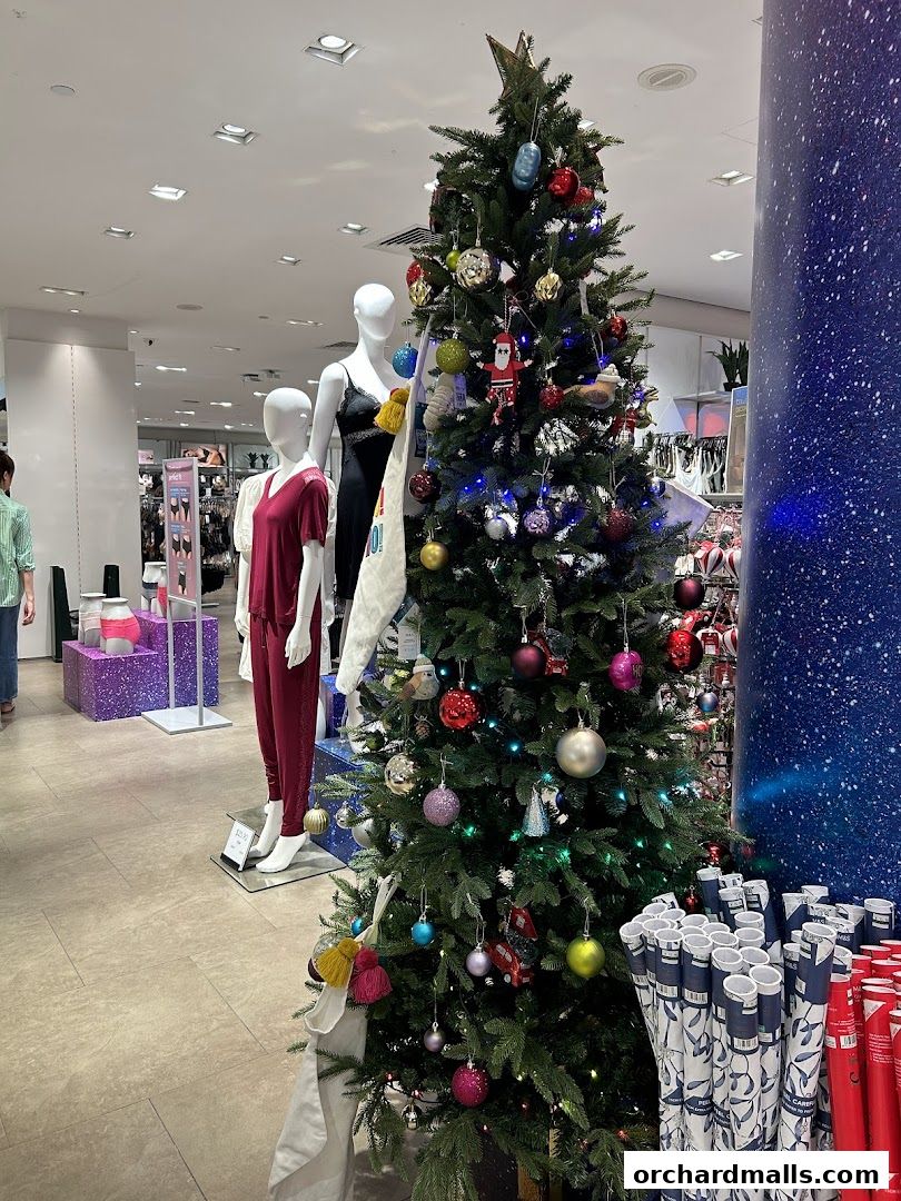 A decorated Christmas tree stands in a Marks & Spencer store, with mannequins and merchandise visible.