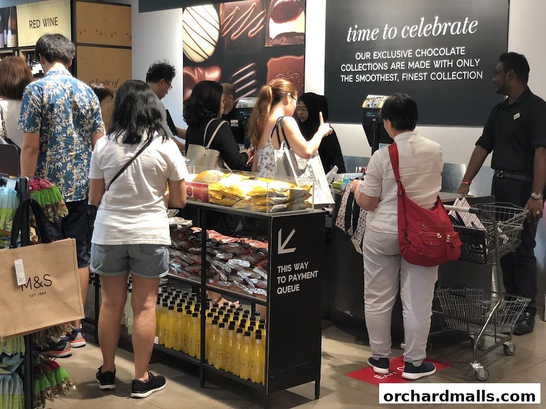 Customers queue at the Marks & Spencer checkout, with chocolate displays and wine visible.