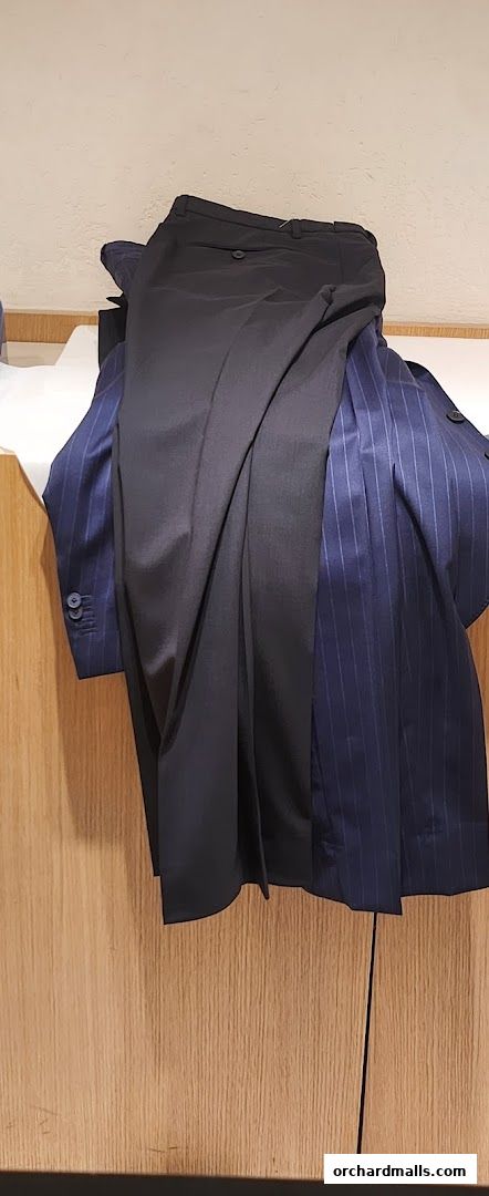 A navy pinstripe suit jacket and black trousers are displayed on a wooden surface.