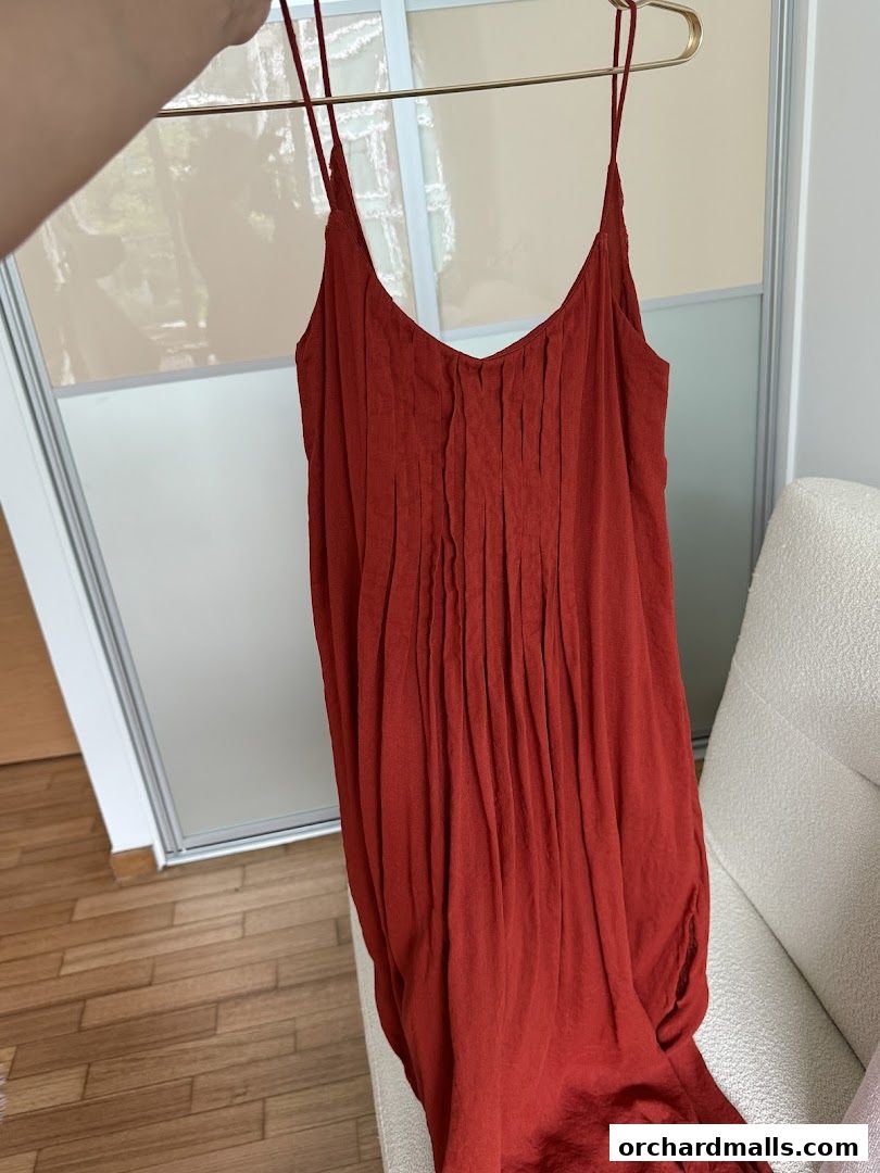 A rust-colored dress with spaghetti straps and a pleated bodice is displayed.