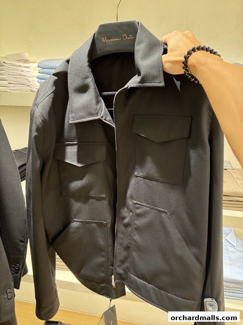 A person holds up a black Massimo Dutti jacket with multiple pockets.