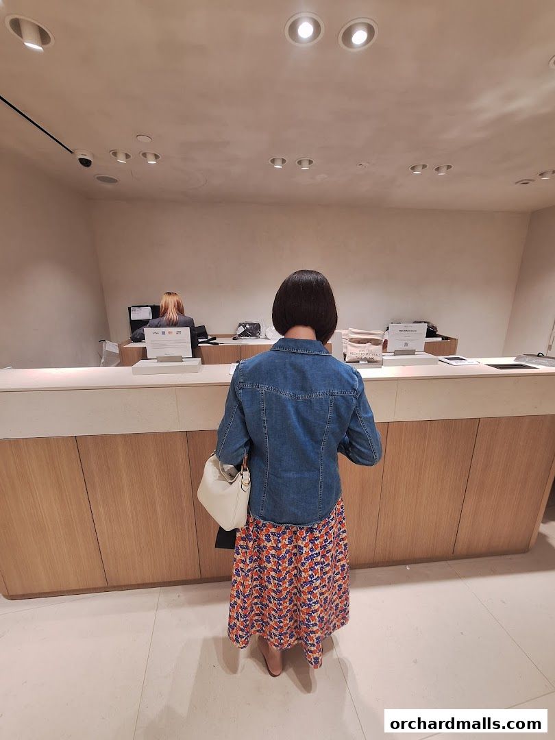A customer stands at the counter of a Massimo Dutti store, with staff behind the counter.