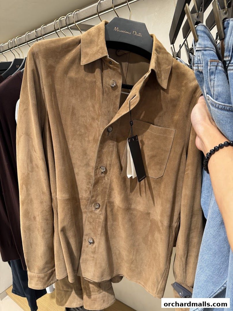A suede shirt from Massimo Dutti on a hanger, with jeans and other clothing in the background.