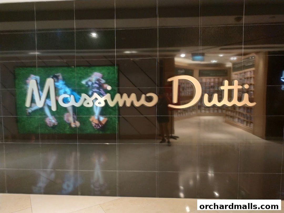 The Massimo Dutti store entrance with its logo and a display featuring people on grass.