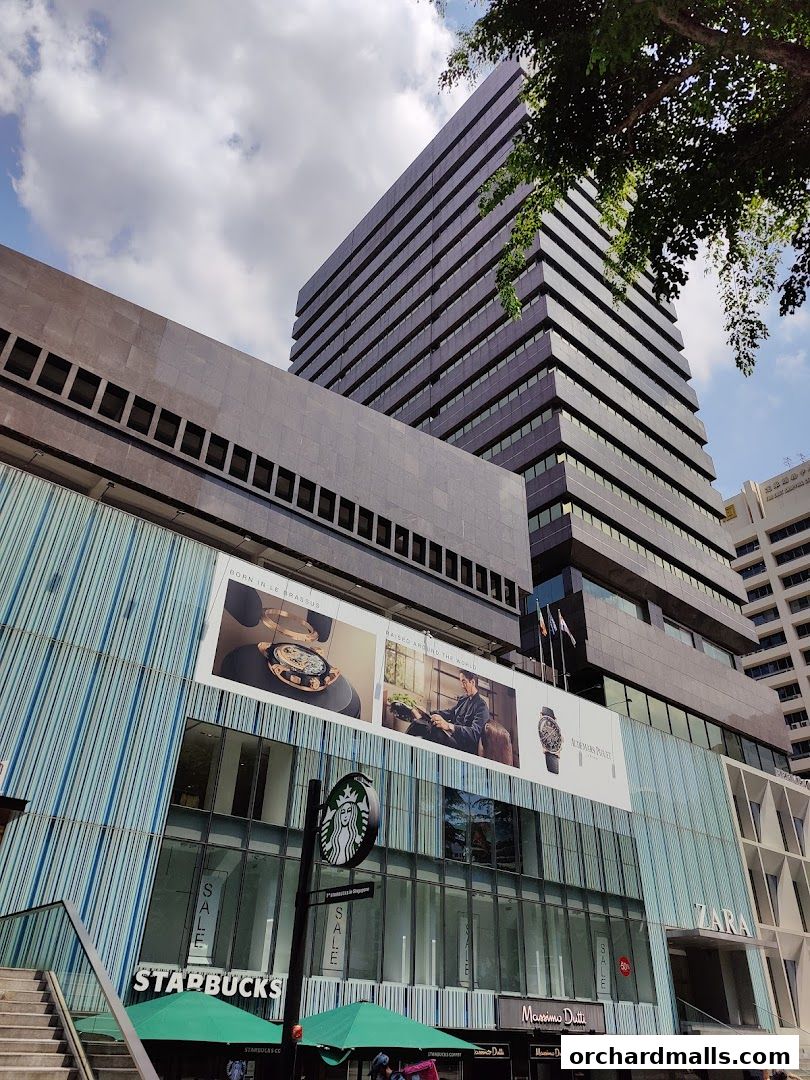 Exterior view of a modern building with multiple retail stores including Starbucks, Zara, and Massimo Dutti.