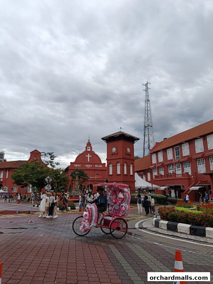 A decorated trishaw waits for passengers in front of historic red buildings under a cloudy sky.