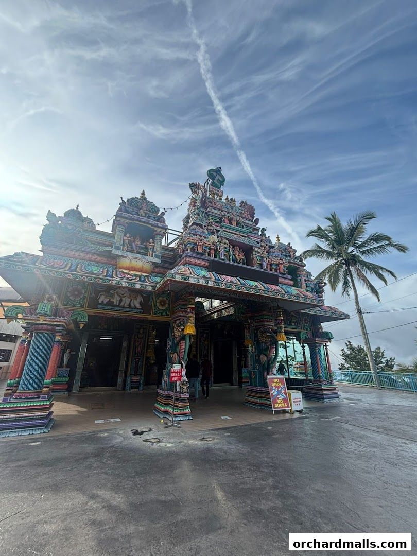 A vibrant Hindu temple entrance with intricate carvings and colorful statues under a cloudy sky.