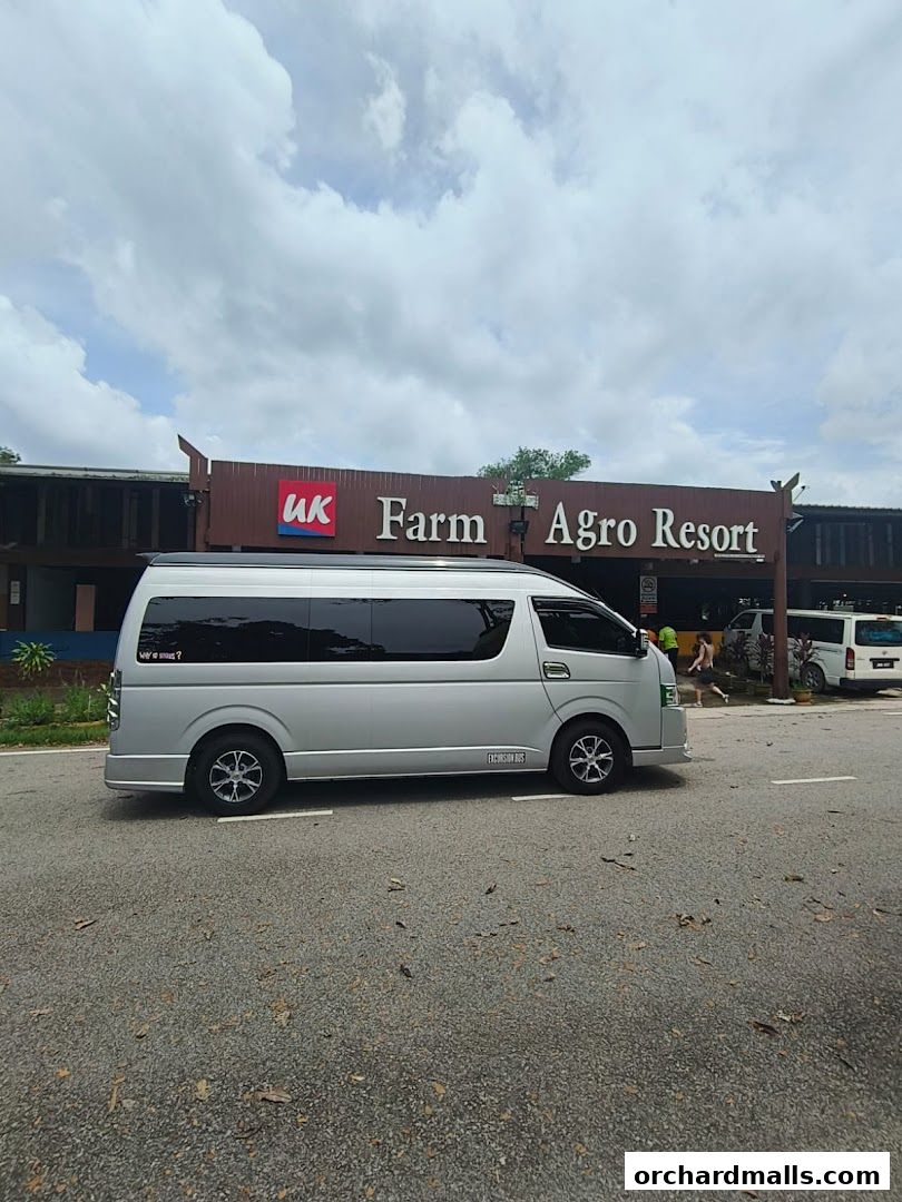 Silver van parked in front of UK Farm Agro Resort entrance with a cloudy sky.