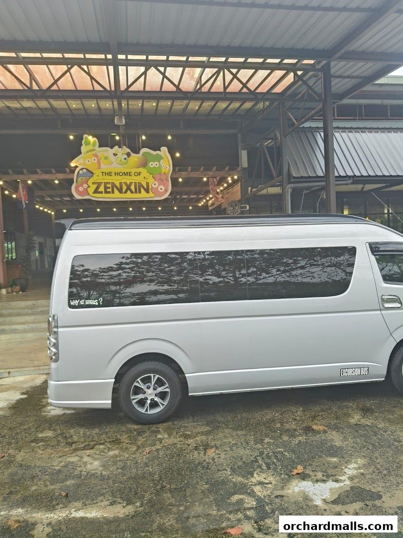 A silver excursion bus parked outside a building with a "The Home of Zenxin" sign.