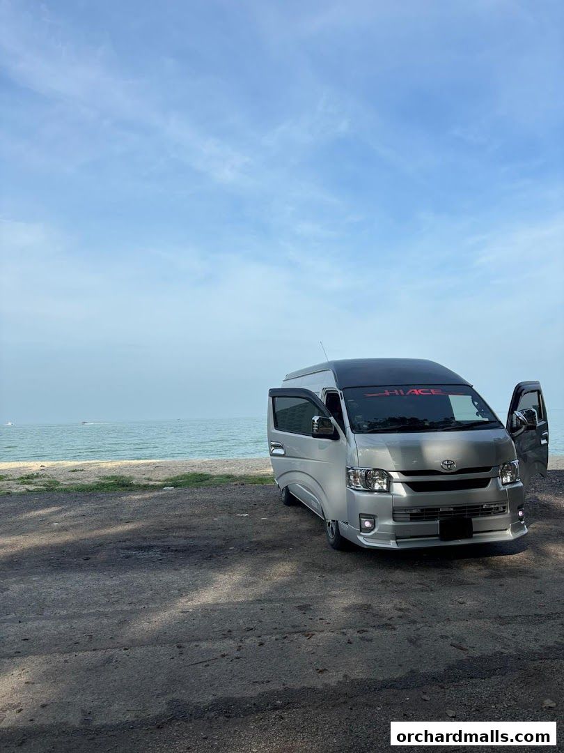 A silver MaxiCabTransit van parked on a beach with the ocean in the background.