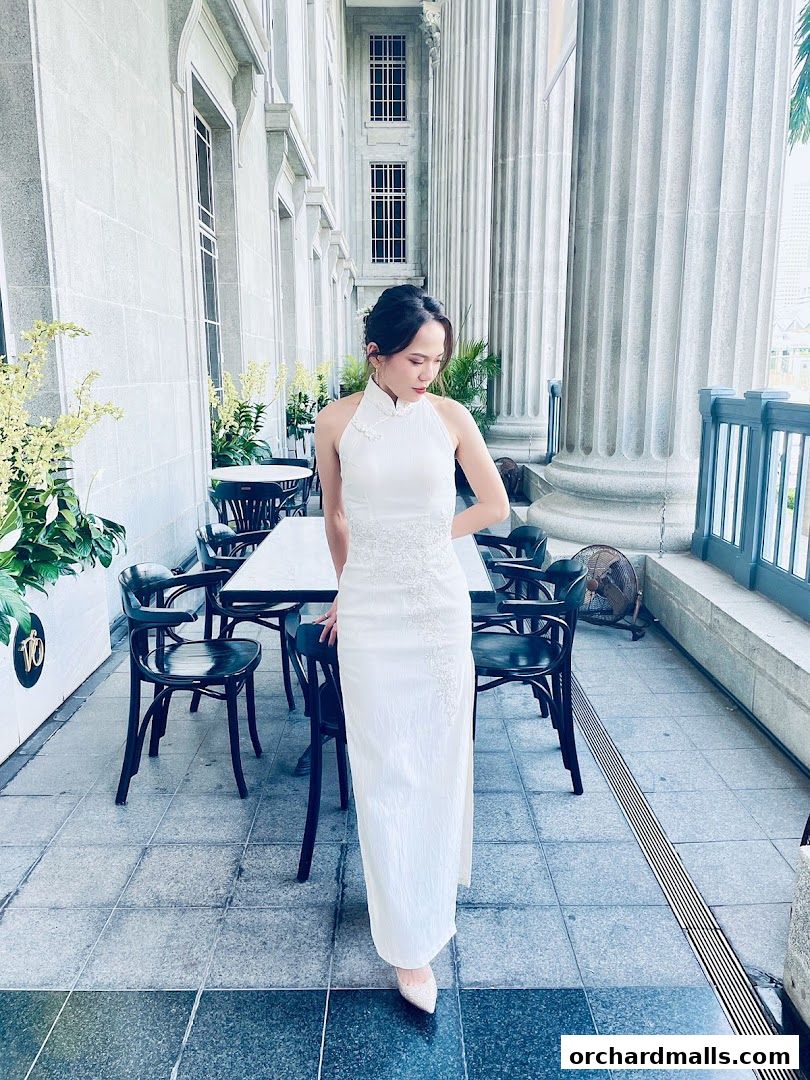 A woman in a white cheongsam stands on a tiled patio with outdoor seating.