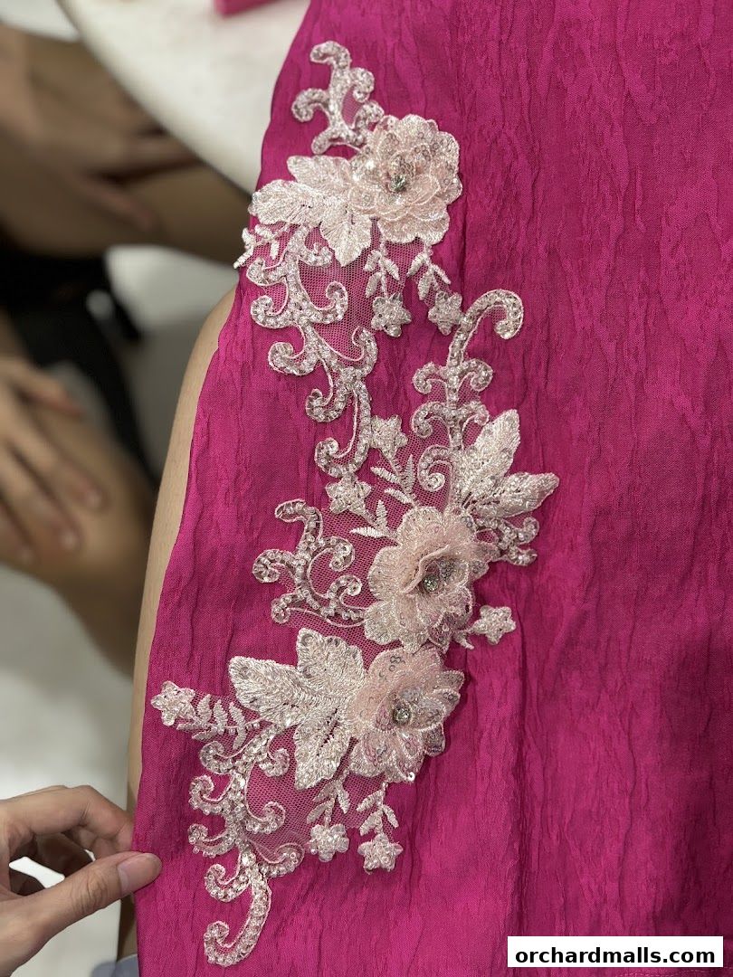 Close-up of a vibrant pink garment with intricate floral lace applique and embellishments.