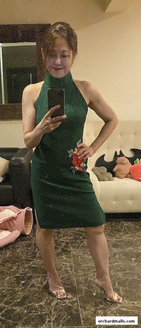 A woman in a green dress with floral embroidery poses for a mirror selfie.
