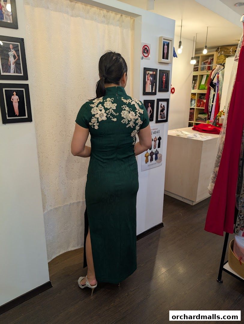 A woman models a dark green cheongsam dress with floral embroidery in a boutique.