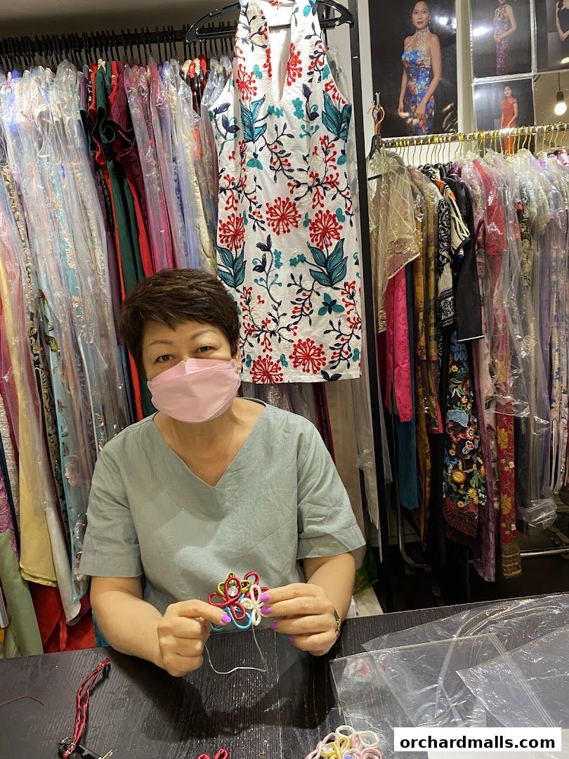 A woman in a pink mask is crafting a colorful accessory amidst racks of dresses.