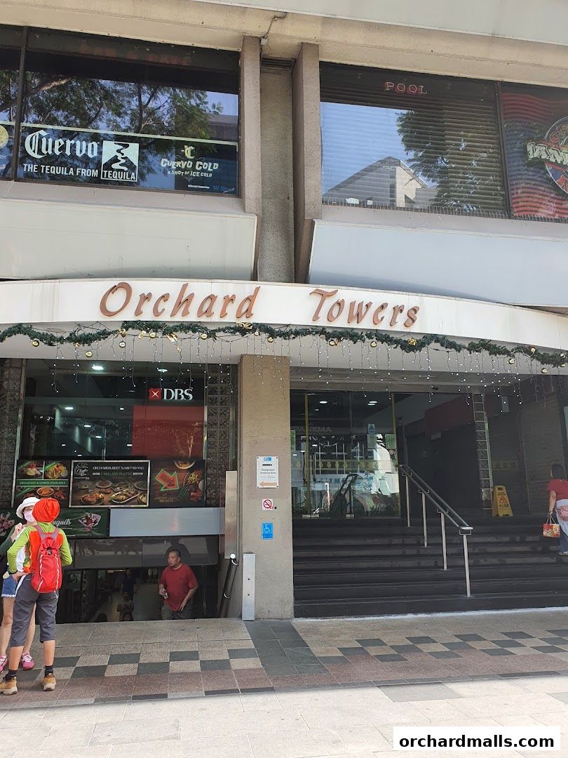 The entrance to Orchard Towers building with various shops and signs visible.