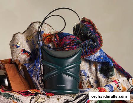 A dark green leather bucket bag with criss-cross detailing, displayed with textured fabrics.