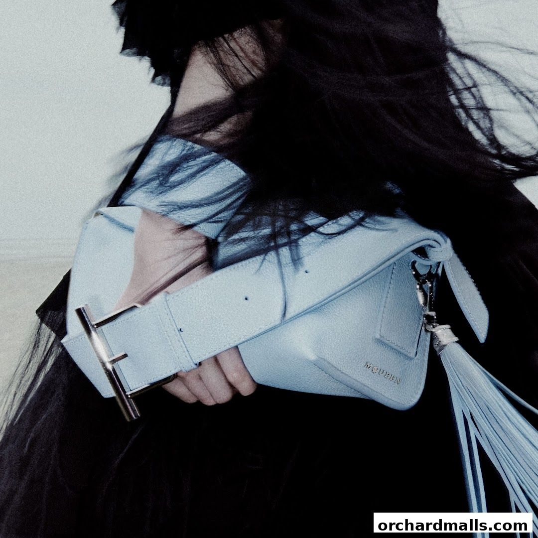 A person holds a light blue leather handbag with a tassel and a prominent buckle.