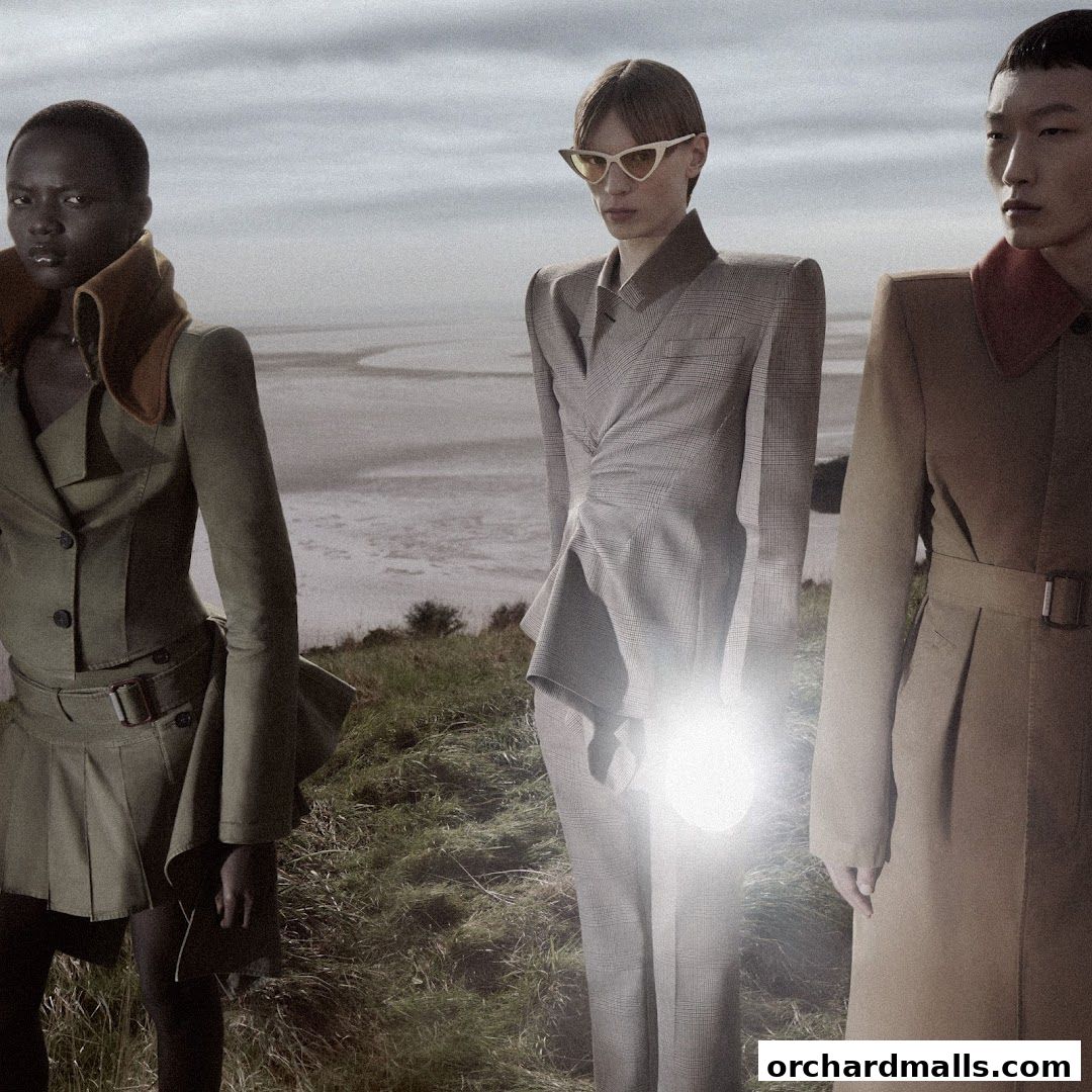 Three models in avant-garde fashion stand in a grassy, outdoor landscape.