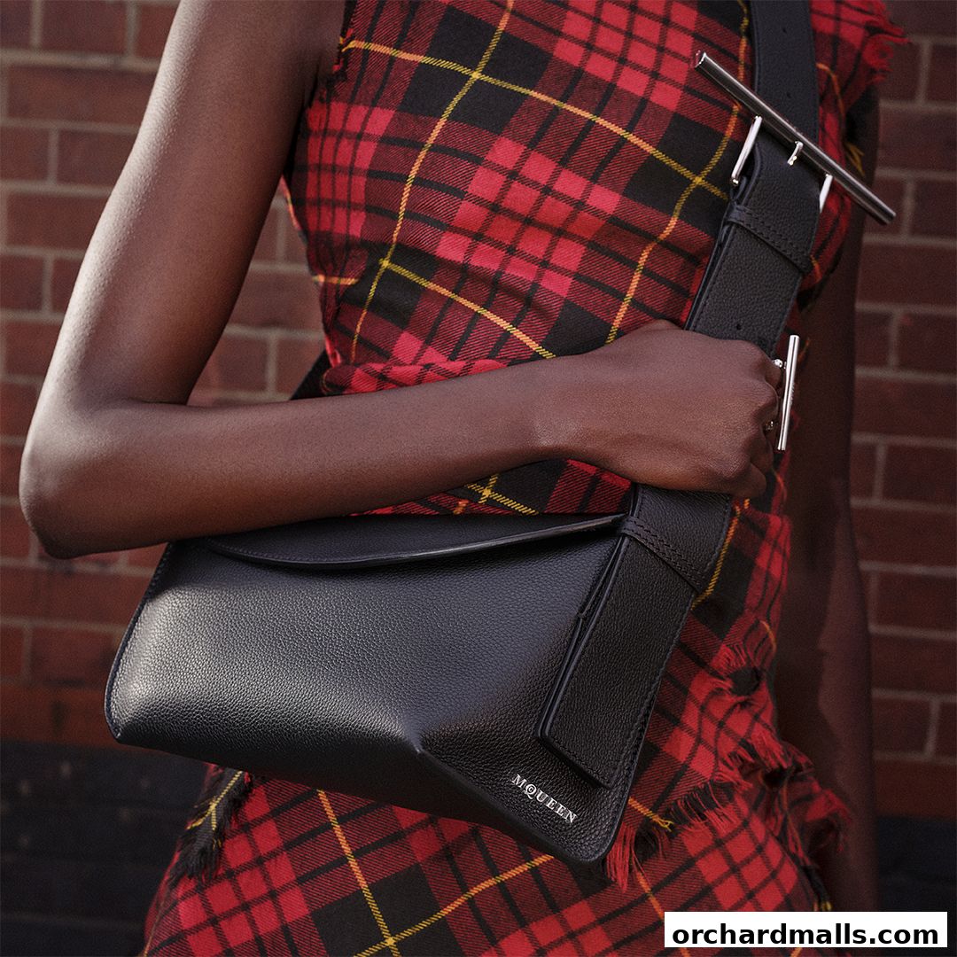 A person wearing a red plaid dress holds a black leather McQueen handbag.