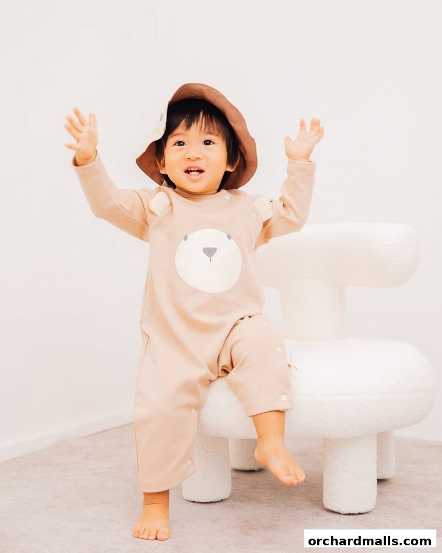 A happy toddler in a bear-themed romper and hat sits on a fluffy white chair.