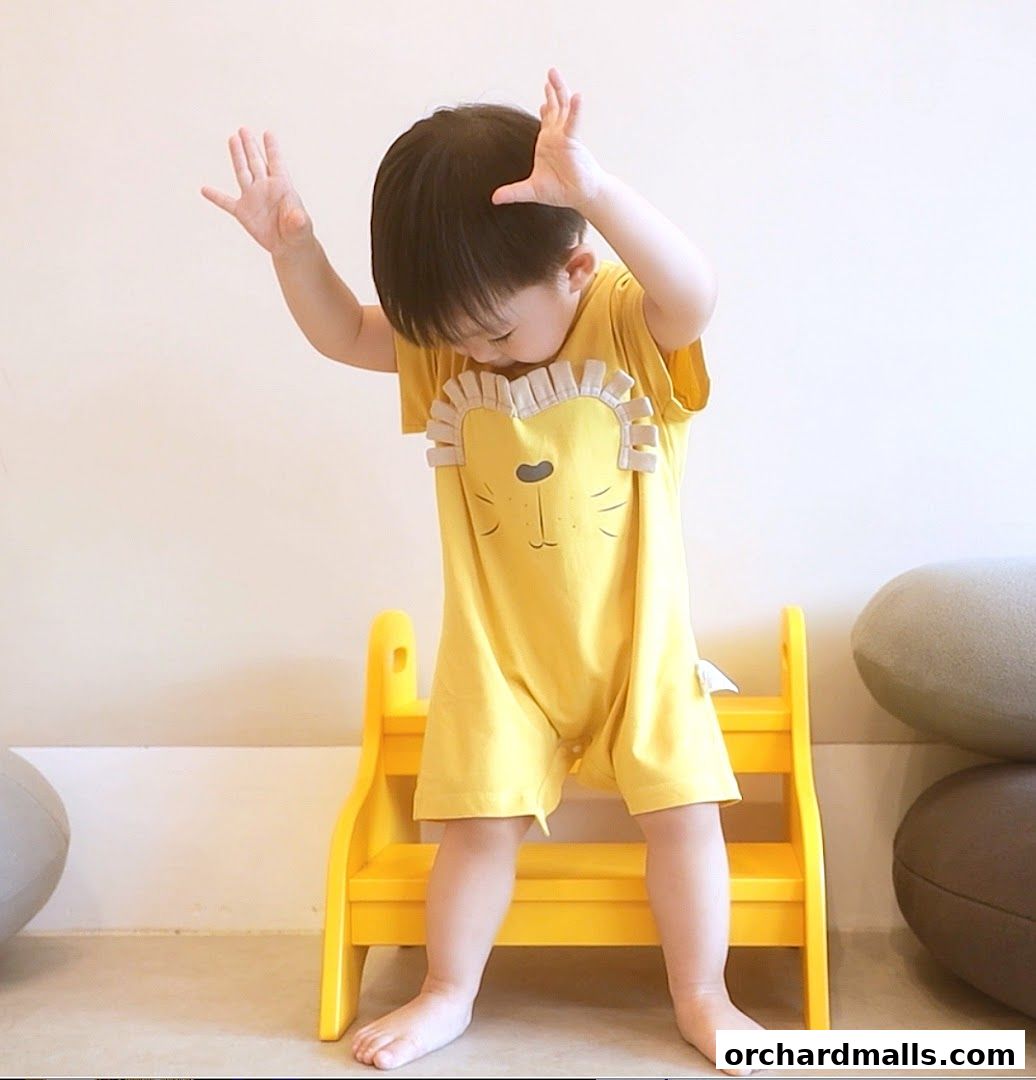 A child in a yellow lion-themed romper stands on a yellow step stool.