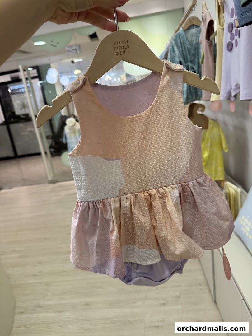 A child's pastel-colored romper with a textured fabric hangs on a wooden hanger.