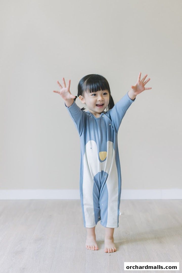 A happy young child in a cute blue penguin-themed romper with arms outstretched.