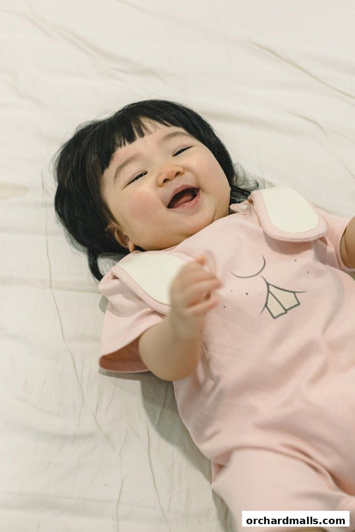 A happy baby in a pink bunny-themed romper lies on a white surface.